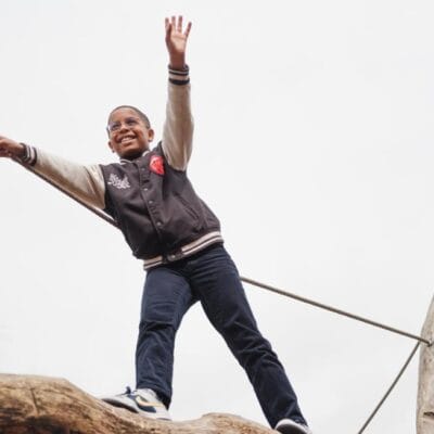 jongen met bril loopt op boomstam