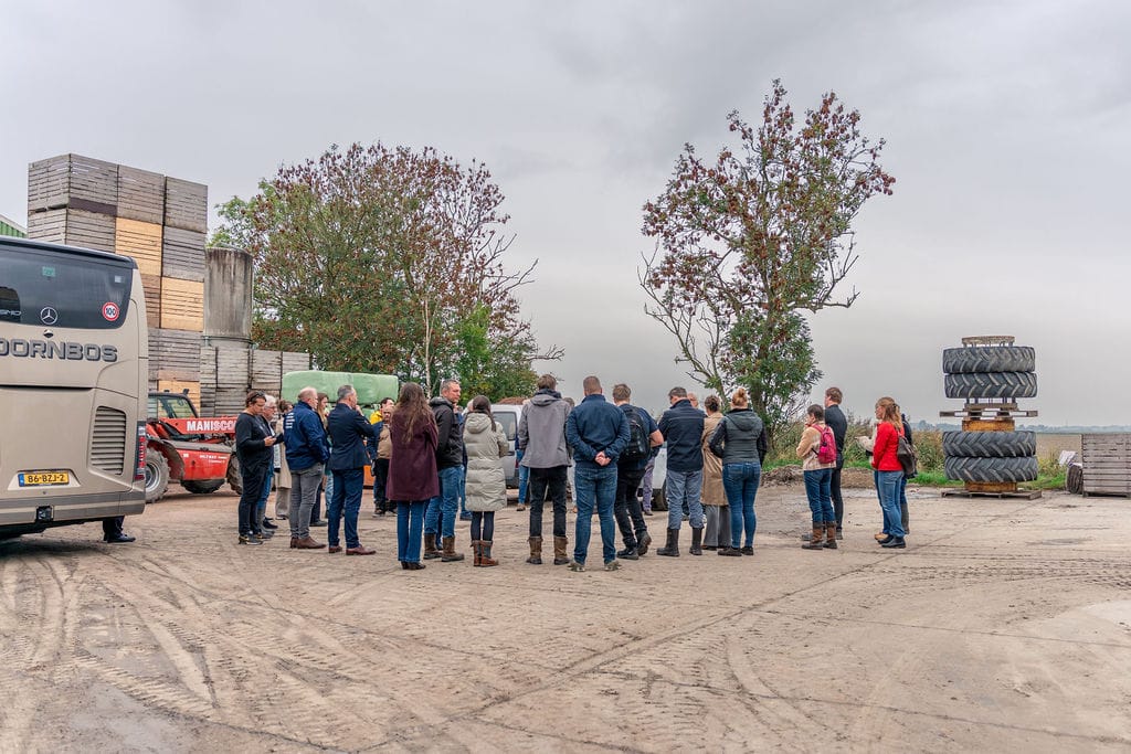 Bezoekers van Agrotour staan in een groep op een boerenerf bij de bus