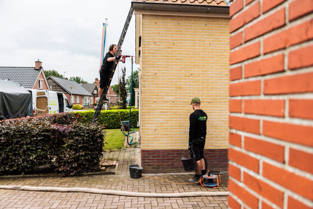 Medewerker isolatiebedrijf isoleert spouwmuur vanaf ladder